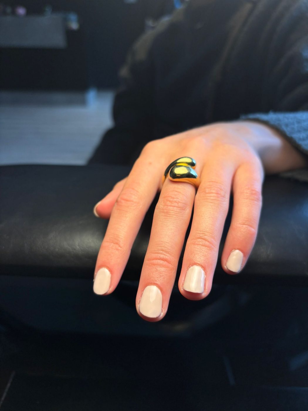 Een hand met naturel nagels met witte toppen en een ring, op een zwarte armleuning